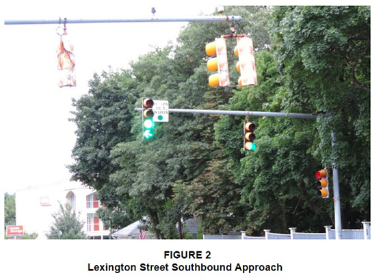Figure 2. Figure 2 is titled "Lexington Street Southbound Approach.” It is a photograph taken from the perspective of a southbound driver approaching the traffic signal at the intersection. The traffic signal has a solid-green ball and, below it, a green left-turn arrow, indicating that a driver may make a protected left turn.