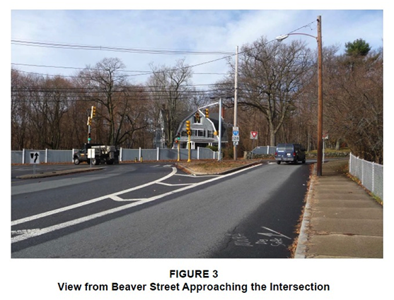 Figure 3. Figure 3 is titled “View from Beaver Street Approaching the Intersection.” It is a photograph taken from the perspective of a driver approaching the intersection. It shows that the two-lane approach is split by a triangular median.