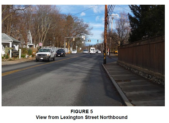 Figure 5. Figure 5, titled “View from Lexington Street Northbound,” is a photograph taken from the perspective of a driver traveling northbound. It shows the road ahead, some cars on the road, and some trees and houses at the sides of the road.